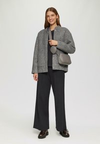 Grijze textuurjack, zwarte top, wijde zwarte broek en bruine brogueschoenen. Grijze schoudertas met ronde vorm en band.