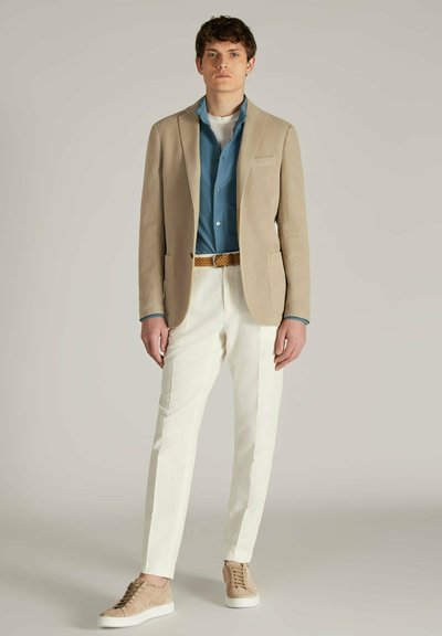 Beige blazer over een lichtblauw shirt, witte trousers en beige suède sneakers. Opvallende details: zakken op de blazer en een gevlochten riem.