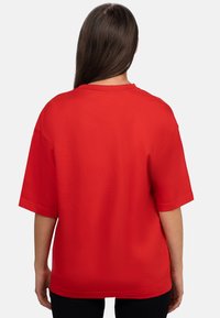 T-shirt rossa oversize con maniche corte, scollatura rotonda e una superficie liscia e uniforme; la vista dal retro rivela una vestibilità comoda.