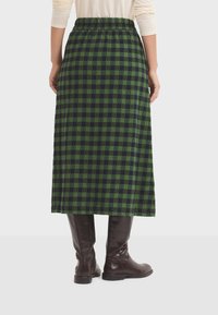 Falda de longitud media de cuadros en verde y azul marino con cinturilla elástica; combinada con botas altas de chocolate brillantes, de textura suave.