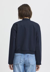 Sweatshirt court bleu marine avec col et poignets côtelés, présentant une texture lisse et des épaules tombantes. Assorti à un jean bleu clair.