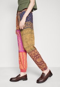 Pantalones de varios colores con estampados de paisley en tonos de azul, dorado, rosa y marrón, con puños elásticos y un ajuste holgado.