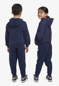 Conjunto de hoodie e calças azul marinho, feito de tecido suave. Apresenta um capuz, punhos elásticos e cintura franzida. Os ténis têm detalhes brancos.