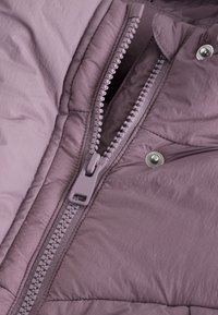 Puhvisjope pehmeast lavendlivärvisest kangast, mis on varustatud silmatorkava tõmblukuga ja hõbedase kinnituse detailiga. Tekstureeritud pind kergelt polsterdatud.