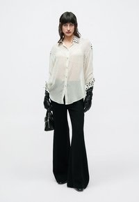 Balta caurspīdīga kreklveida krekls ar melniem punktiņiem, ar punktiņu apkakli un aprocēm. Kopā ar melnām platām biksēm un melnām cimdiem.