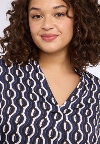 Bluzka z kołnierzykiem w geometryczny wzór w kolorach granatowym, kremowym i czarnym; gładka tkanina z delikatnym połyskiem; posiada dekolt w serek i subtelne marszczenia.
