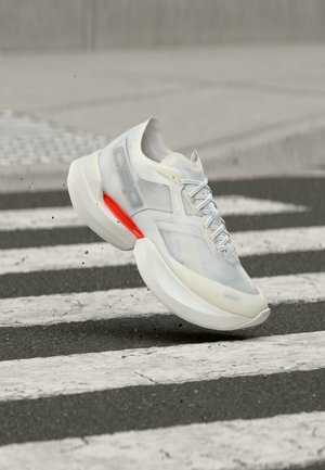 White modern sneaker with red accent floats above a zebra crossing, kicking up small debris on an urban street.