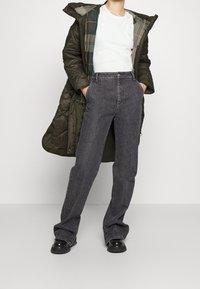 Pufová bunda v tmavě olivové barvě, s prošívanou texturou a kostkovanou podšívkou. Spárována s vysokým pasem, rovným střihem černými džínami a černými botami.