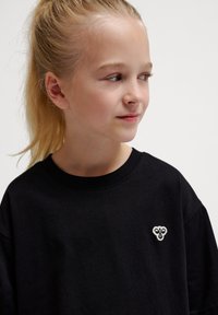 Schwarzes Baumwoll-T-Shirt mit rundem Ausschnitt und einem kleinen weißen gestickten Design auf der linken Seite. Weicher Stoff und lässige Passform.