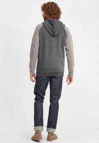 Gray hoodie with light gray sleeves, kangaroo pocket, and drawstring hood. Worn with dark denim jeans and beige ankle boots. Plain background.