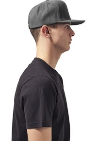 Casquette de baseball grise présentée de profil, avec un design structuré et un écran plat. Portée avec un t-shirt noir à manches courtes.