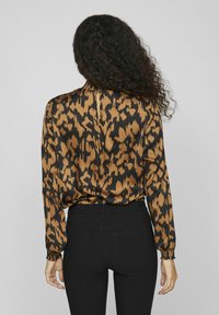 Blouse en imprimé léopard marron et noir avec des manches longues et un col haut, portée avec un jean noir ajusté. Texture de tissu lisse.