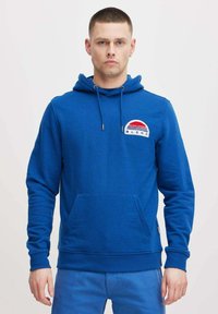 Felpa con cappuccio blu, tasca frontale, cordino e logo ricamato con strisce rosse e bianche in un design circolare.