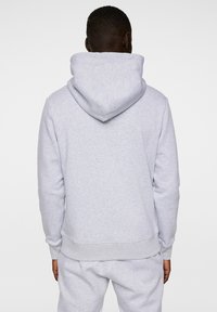 Grå sweatshirt med huva, tillverkad av mjukt material. Har en ribbad kant nertill och vid ärmarna, och verkar ha en avslappnad passform. Inga synliga mönster eller detaljer.