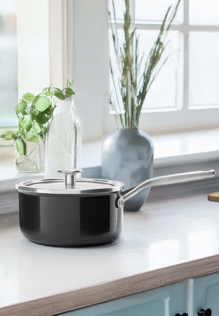 Casserole noire avec un couvercle et une poignée en acier inoxydable, dotée d'une finition lisse et d'une forme ronde, posée sur un comptoir.