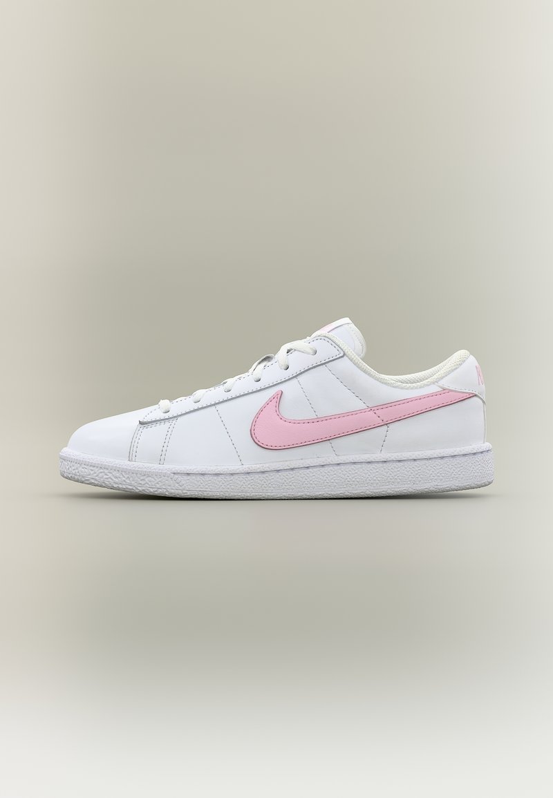 Baskets basses blanches avec virgule Nike rose et lacets, semelle en caoutchouc texturée blanche, présentées sur un fond clair neutre.