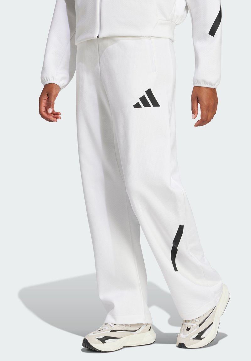 Baltas sporta bikses, izgatavotas no gludas auduma, ar melnu Adidas logotipu un abstraktiem akcenteiem. Brīva piegriezuma ar sānu kabatām funkcionālitātei.