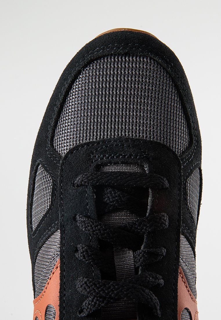 Scarpa sportiva nera con una tomaia testurizzata, pannelli in rete e accenti arancioni. Presenta un design con lacci e una suola in gomma di contrasto.