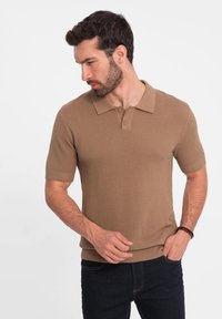 Pánský polo triko s krátkým rukávem ve světle hnědé barvě, vyrobené z texturovaného materiálu, s klasickým límečkem a dvoupolohovým zapínáním na knoflíky.