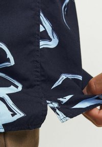Camicia a maniche corte con tessuto blu navy e un motivo astratto azzurro, caratterizzata da un orlo cucito e una texture liscia.