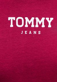 Červená bavlněná mikina s bílým nápisem "TOMMY JEANS" výrazně umístěným na přední straně. Měkká textura a ležérní design.