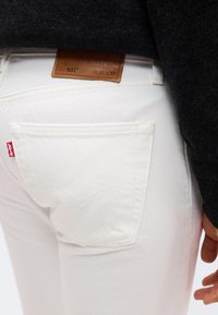 Κοντινό πλάνο στην πίσω τσέπη λευκών τζιν Levi's 501 και καφέ δερμάτινη ετικέτα με μέγεθος μέσης και μήκους, φορεμένα με μαύρο πουλόβερ.