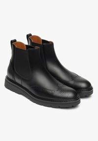 Des bottes de cheville en cuir noir présentent des panneaux latéraux élastiques, des détails de brogue, un bout rond et une semelle en caoutchouc épaisse pour une meilleure adhérence.