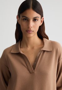 Pullover marrone con colletto e scollatura a V, caratterizzato da un accento metallico testurizzato lungo il collo. Tessuto liscio e morbido con una vestibilità rilassata.