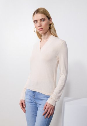 Lyse beige langermet genser med v-hals og myk tekstur, kombinert med lyseblå jeans. Minimalistisk design, tettsittende silhuett.