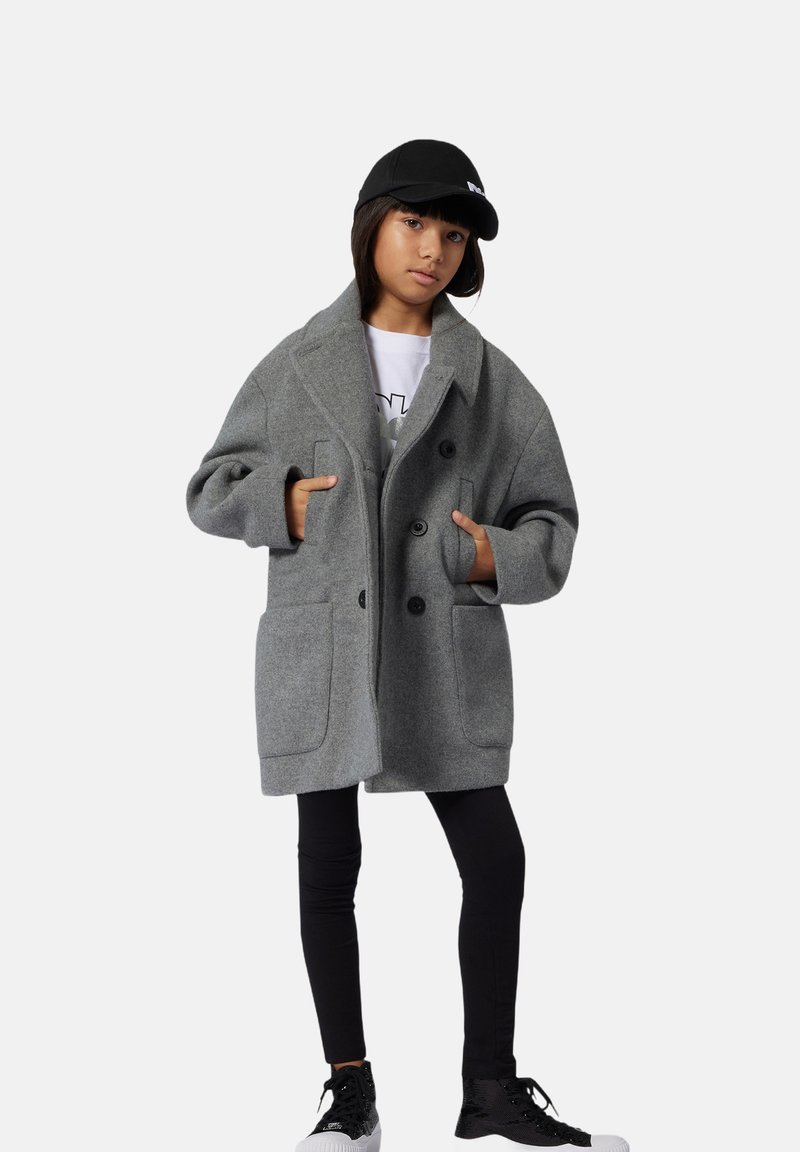 Szary płaszcz z mieszanki wełny o podwójnym zapięciu, z dużymi kieszeniami i klapami, noszony na czarne legginsy i sneakersy.