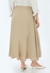 Jupe maxi beige fluide avec une taille élastique. Texture lisse, ourlet arrondi, associée à des chaussures à talons blancs et à bout pointu.