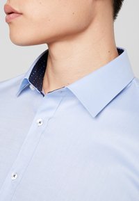 Lichtblauw overhemd met een gestructureerde kraag en een marineblauwe polka dot voering. Voorzien van witte knopen en een gladde textuur.