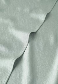 Tessuto verde chiaro e morbido con una texture liscia e lucida, caratterizzato da pieghe delicate e un leggero lucore. Adatto per rivestimenti o abbigliamento.