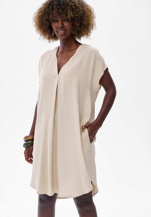 Robe beige à manches courtes avec un décolleté en V, poches latérales et coupe décontractée. Fabriquée en tissu léger avec une texture douce.