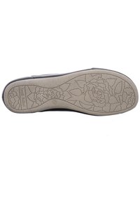 Suela de zapato negra con una parte inferior de goma beige texturizada que presenta un patrón floral. Nombre de la marca impreso en el lateral.