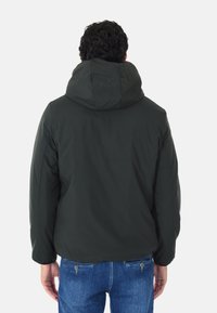 Giacca nera imbottita con cappuccio, caratterizzata da una texture liscia e polsini elastici, indossata con jeans in denim blu. Vista dal retro mostra un design semplice.