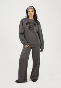Sweatshirt gris avec un motif "New York" et une coupe décontractée, associé à un pantalon large gris assorti ; tissu doux et style décontracté.
