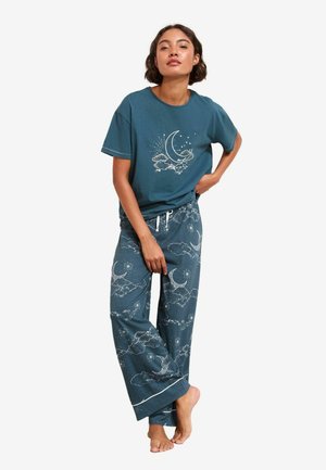 Loungewear-Set aus Baumwolle mit einem türkisfarbenen, oversized T-Shirt mit einem Mond- und Wolkenmotiv sowie passenden, locker sitzenden Hosen mit ähnlichen Mustern.