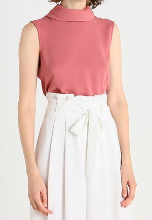 Mouwloze top in stofroze met een hoge hals, gecombineerd met een witte rok met hoge taille en een ceintuur met strik.