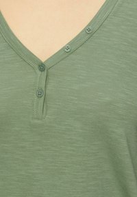Olijf groene katoenen shirt met een V-hals, een drieknoopsluiting en een gestructureerde stof met een gemêleerd patroon.