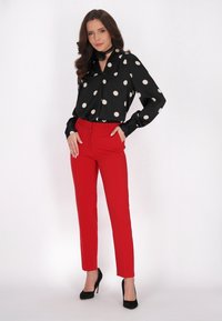 Blusa nera a pois con colletto, abbinata a pantaloni rossi sartoriali. Tacchi alti neri. Tessuto liscio con un design strutturato.