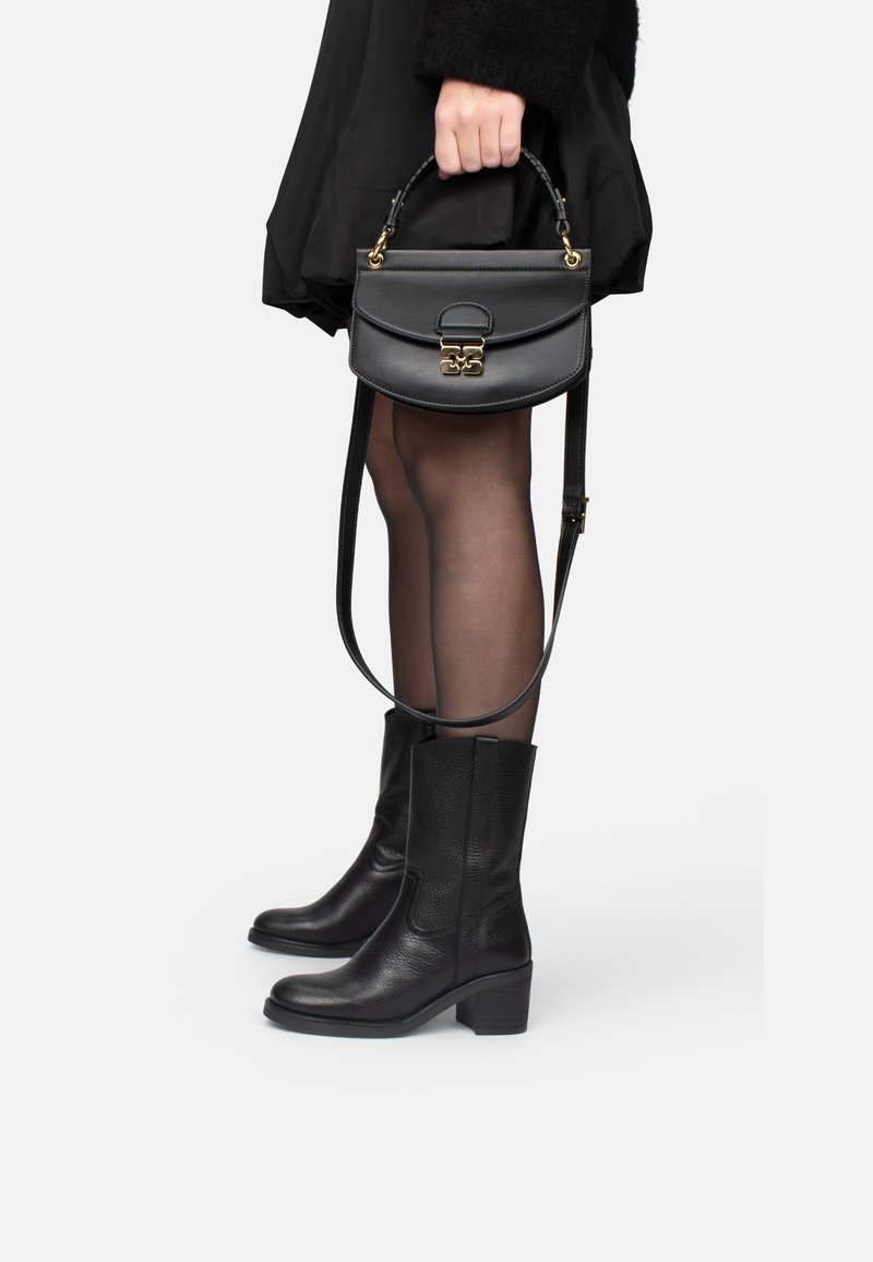 Bolso de mano de cuero negro con un cierre dorado y asa superior, combinado con botas altas de cuero negro texturizadas y medias negras transparentes.