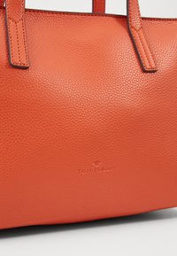 Pomarańczowa torba typu tote ze skóry o ziarnistej fakturze, wyposażona w dwa solidne uchwyty oraz wytłoczone logo "TOM TAILOR" na przodzie.