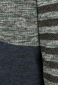 Mnohobarevný textil s texturovaným zeleným a šedým úpletem, který obsahuje pruhované černobílé vzory a pod ním část v jedné barvě námořnické modři.