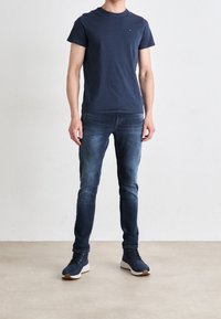 Mörkblå t-shirt med rund hals, slim-fit mörk denimjeans och mörkblå träningsskor. Enkelt mönster med minimal logotyp på t-shirten.