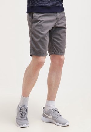Shorts gris en tissu mélangé coton, offrant une coupe décontractée, des poches latérales et un ourlet simple. Portés avec des chaussures de sport grises et des chaussettes blanches.