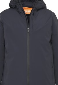 Giacca impermeabile blu navy con cappuccio, dotata di chiusura centrale con zip, due tasche laterali e un logo arancione all'interno del colletto.