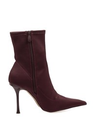 Botín burdeos de tela elástica con punta afilada y tacón alto de aguja. Presenta un cierre lateral y detalles de costura.