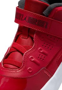 Scarpa sportiva rossa con upper sintetico lucido, dettagli testurizzati, colletto imbottito e una striscia con dettagli del logo nero.