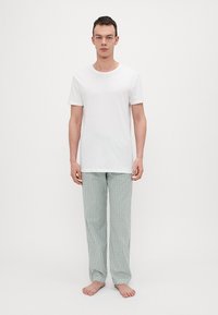 T-shirt en coton blanc associé à un pantalon de pyjama à carreaux verts. Le pantalon a une coupe décontractée et une taille élastique. Pieds nus.